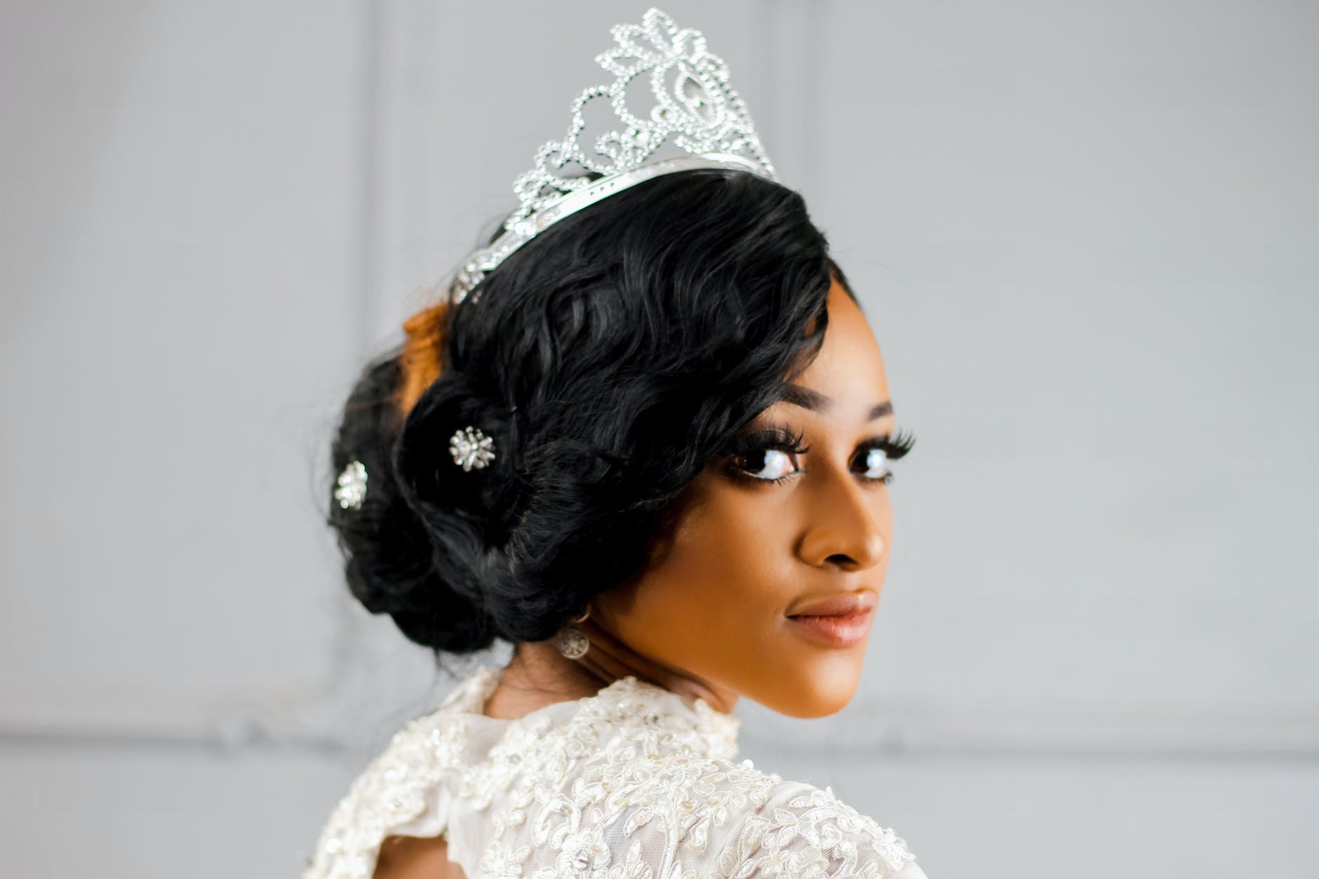 Image is of a Black woman wearing an embellished white dress, with hair pinned up and a jeweled tiara.